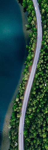 Aerial view of winding road between blue lake and forrest greenery