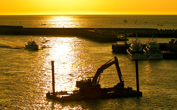 Construction equipment on water barges against sunset