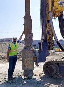 Geotechnical engineer in yellow vest standing next to large ground drill