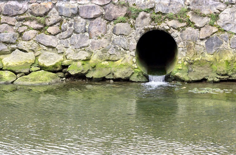 Drainage pipe on a stone wall with green mud.