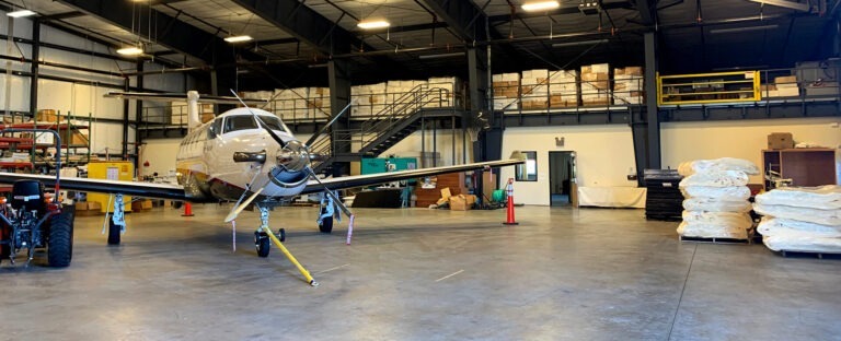 Photo of inside an airplane hanger with a white airplane parked inside.