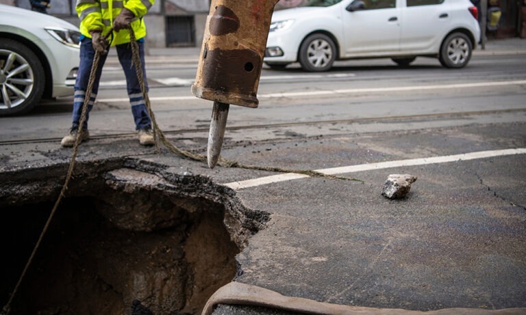 A worker standing next to a large hole on a city street.